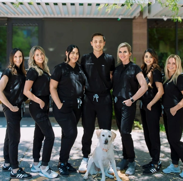Team photo of BCR Dentistry staff standing together outdoors with a small dog