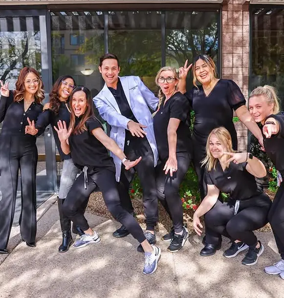 Dr. Brandon Harris and the dental team smiling outside the Biltmore Cosmetic & Restorative Dentistry clinic in Phoenix, next to a list of dental frequently asked questions.