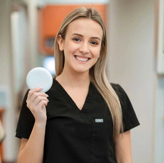A smiling dental assistant in black scrubs holding a white Invisalign case, next to text about clear aligners at Biltmore Cosmetic & Restorative Dentistry in Phoenix.