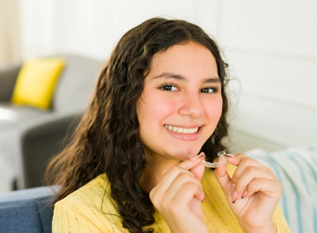 A smiling teenage girl holding clear orthodontic aligners next to web copy explaining Invisalign Teen treatment options in Phoenix.