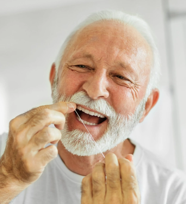 A senior man smiling while flossing his teeth next to text about the importance of routine dental care and checkups at Biltmore Cosmetic & Restorative Dentistry in Phoenix.